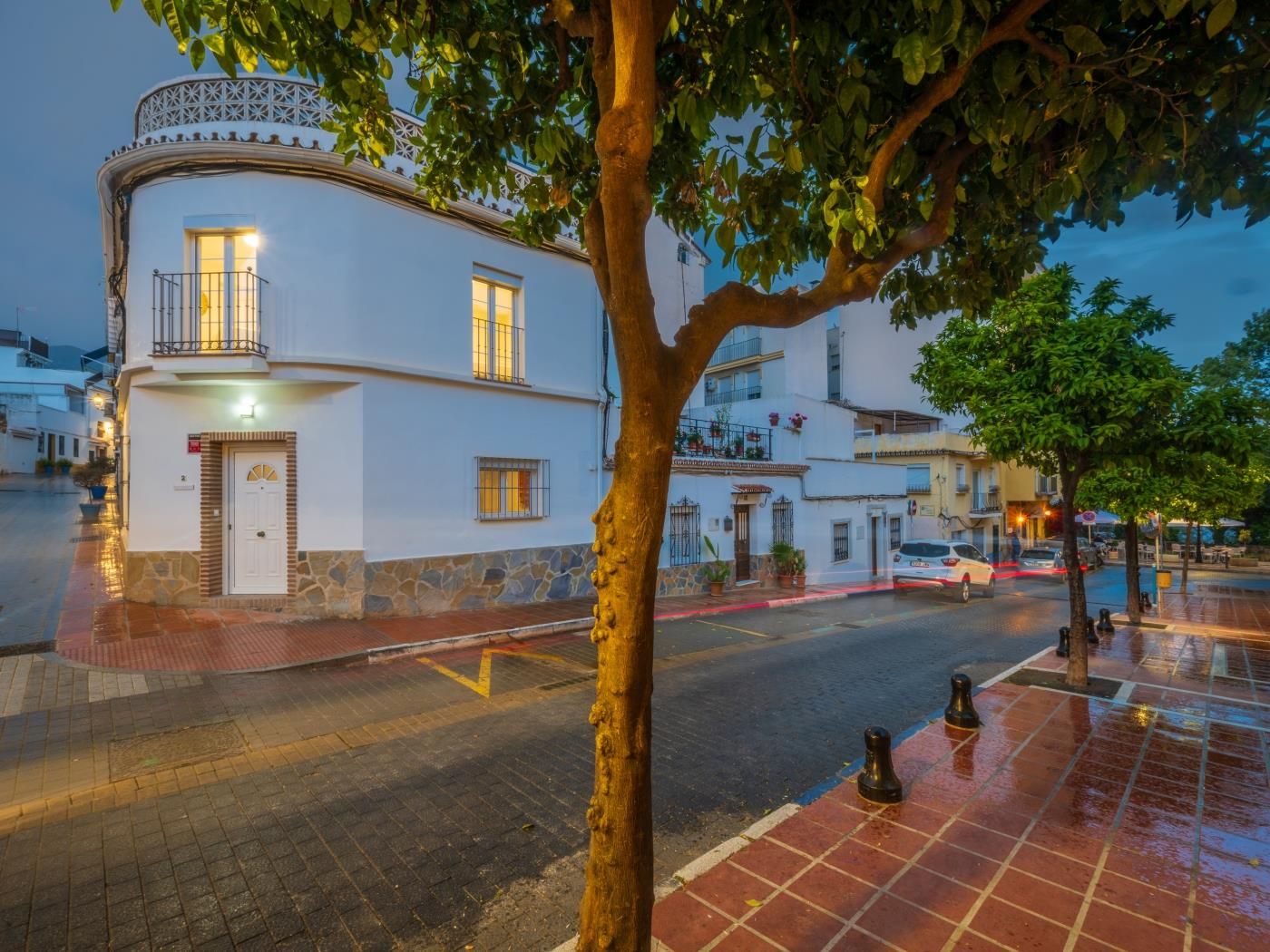 Whitewashed townhouse on a cobblestone street with orange trees in Marbella Old Town at dusk